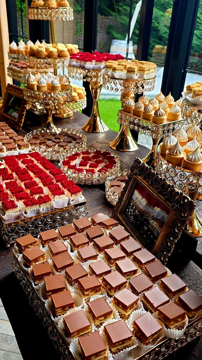 Candy bar DulciSsima aranjat la un eveniment, cu monoporții roșii, felii cu ciocolată și bezele pe suporturi aurii